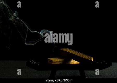 Palo Santo beleuchtet mit Rauch auf dunklem Hintergrund horizontal zur Meditation Stockfoto