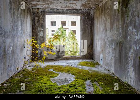 Verlassenes, beschädigtes Zimmer mit Blick nach draußen durch ein Loch anstelle eines Balkons in einem Paneelhaus. Stockfoto