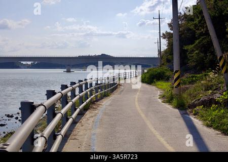 Muan County, Südkorea - 25. September 2020: Ein schmaler Abschnitt des Yeongsangang Bike Path schlängelt sich entlang des Flusses und führt unter einer modernen Brücke vorbei. Stockfoto