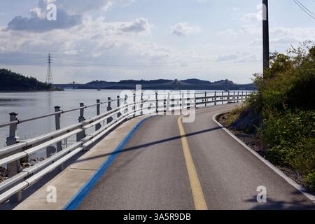 Muan County, Südkorea – 25. September 2020: Ein gewundener Abschnitt des Yeongsangang Bike Path verläuft am Ufer des Wassers entlang, wobei eine Brücke über den Fluss führt Stockfoto