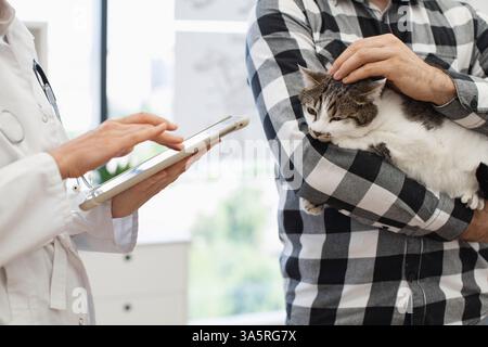 Tierarzt mit Tablette, um medizinische Vorgeschichte oder Verschreibung für den Mann mit Katze zu erklären. Das Bild zeigt Unterstützung, Tierpflege und Interaktion mit fortschrittlicher Technologie Stockfoto