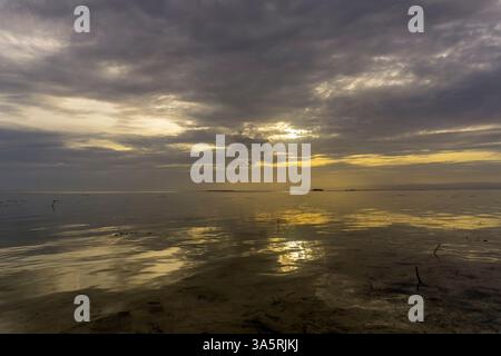 Sonnenuntergang über ruhigem Wasser mit Reflexionen und dramatischen Wolken Stockfoto