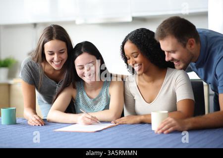 Vier glückliche Mitbewohner, die den Vertrag in der Küche zu Hause überprüfen Stockfoto