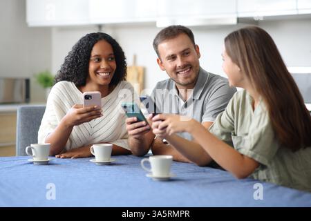 Drei interrassische Freunde überprüfen ihre Smartphones und unterhalten sich zu Hause Stockfoto