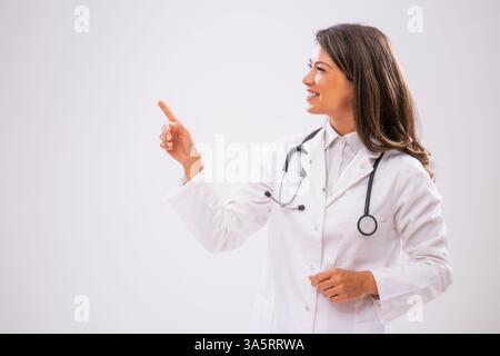 Das Studio hat ein Porträt einer fröhlichen Ärztin aufgenommen, die auf den Kopf zeigt. Stockfoto