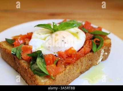 Nahaufnahme mit köstlichem Toast aus frischen Tomaten und Basilikum, garniert mit pochiertem Ei Stockfoto
