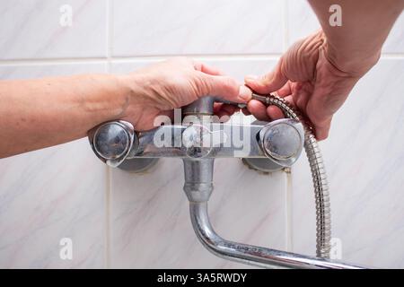 Frau wechselte kaputten Duschschlauch im Badezimmer. Befestigungsschlauch für Klempnerhände mit Innengewinde. Sanitär-Konzept. Das Berufskonzept männlich und weiblich. Stockfoto