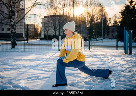 Frau dehnt sich und macht im Winter einen Ausfallschritt im Freien Stockfoto