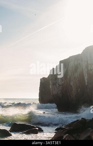 Sonnenbeschienene Klippen mit Meereswellen, die auf Felsen in peniche krachen Stockfoto