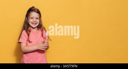 Ein glückliches Mädchen hält eine Zahnbürste in den Händen. Eine isolierte Panoramaaufnahme. Ein Ort für Ihre SMS. Kinderzahnheilkunde Stockfoto