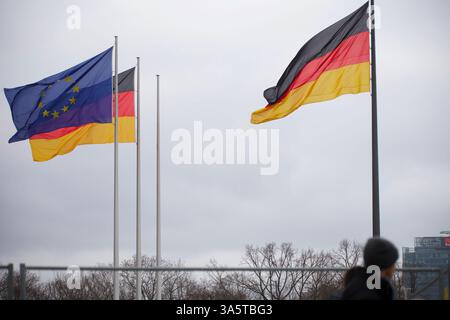 Berlin, Deutschland. Februar 2025. Eine Person läuft vor dem Bundestag an einer deutschen Flagge und einer EU-Flagge. Stockfoto