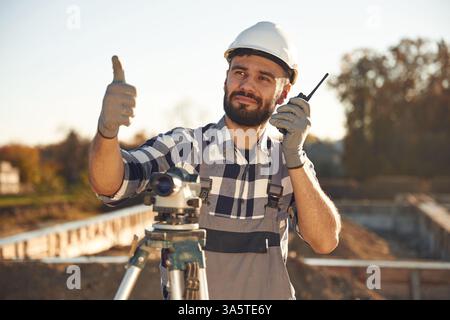 Auf dem Funkgerät, mit geodätischer optischer Ebene. Der Arbeiter ist tagsüber auf der Baustelle. Stockfoto
