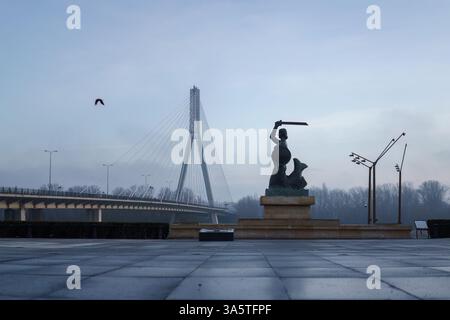 Warschau, Polen. 27. Januar 2025 - Meerjungfrauenstatue mit Swietokrzyski-Brücke im Hintergrund, am frühen Morgen. Stockfoto