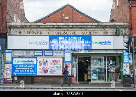 Ein Mann spricht mit seinem Telefon, während er am Big Discount Convenience Store in der Hyde Road, Gorton, Manchester, vorbeiläuft. Stockfoto