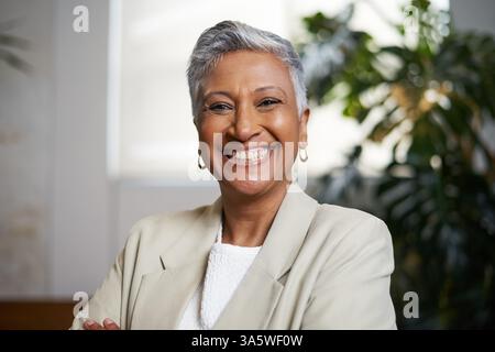 Selbstbewusste Reife lächelt in einer modernen Inneneinrichtung, umgeben von Grün Stockfoto