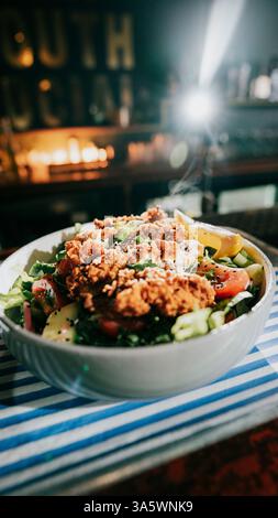 Eine Schüssel Essen mit viel Gemüse und Fleisch. Die Schüssel steht auf einem Tisch mit einer blau-weißen Tischdecke Stockfoto