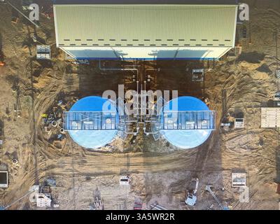 Luftaufnahme einer im Bau befindlichen Industrieanlage mit zwei großen blauen Lagertanks, die mit einer Verarbeitungsanlage verbunden sind. Die Website zeigt Konstr Stockfoto