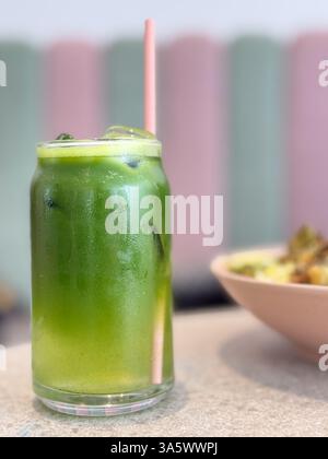 Ein hohes Glas eisgrüner Saft mit rosa Strohhalm, der auf einem Tisch in einem pastellfarbenen Café sitzt Stockfoto
