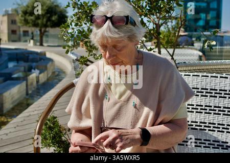Ältere Frau, die ihr Smartphone im Freien bei hellem sonnigem Wetter benutzt Stockfoto