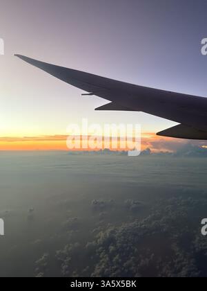 Flugzeugflügel über den Wolken bei Sonnenaufgang aus dem Passagierfenster in einem Flugzeug. Stockfoto