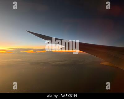 Flügel eines Flugzeugs im Flug während der goldenen Stunde mit Wolken. Luftaufnahme aus dem Flugzeugfenster bei Sonnenuntergang. Stockfoto