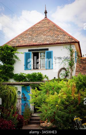 Ein bezauberndes altes Haus mit Terrakotta-Dach, blauen Fensterläden und weißen Putzwänden liegt eingebettet in einen üppigen Garten. Umgeben von Grün und Vibran Stockfoto