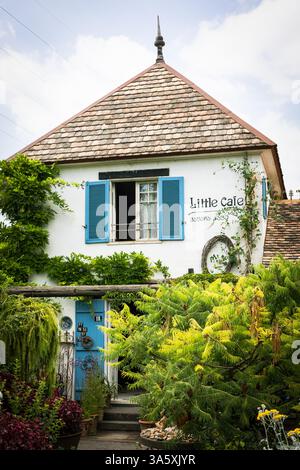 Ein bezauberndes altes Haus mit Terrakotta-Dach, blauen Fensterläden und weißen Putzwänden liegt eingebettet in einen üppigen Garten. Umgeben von Grün und Vibran Stockfoto