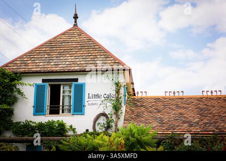 Ein bezauberndes altes Haus mit Terrakotta-Dach, blauen Fensterläden und weißen Putzwänden liegt eingebettet in einen üppigen Garten. Umgeben von Grün und Vibran Stockfoto