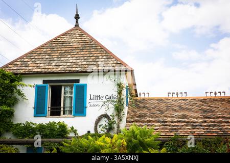 Ein bezauberndes altes Haus mit Terrakotta-Dach, blauen Fensterläden und weißen Putzwänden liegt eingebettet in einen üppigen Garten. Umgeben von Grün und Vibran Stockfoto