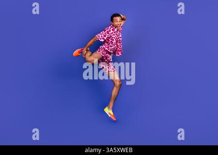 Mann, der auf purpurnem Hintergrund springt und rosa Leopardenkleidung trägt Stockfoto