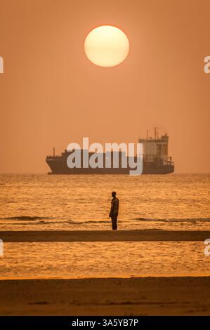 Ein Frachter fährt entlang der Küste von Merseyside vorbei an „Another Place“, einer Skulptur von Sir Antony Gormley am Crosby Beach. Stockfoto