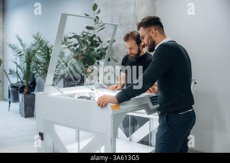 Zwei Männer stehen und arbeiten am 3D-Drucker. Stockfoto