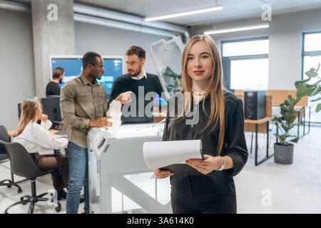 Frau steht vor Kollegen. Die Leute sind im Büro am 3D-Drucker. Stockfoto