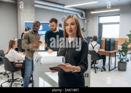 Frau steht vor Kollegen. Die Leute sind im Büro am 3D-Drucker. Stockfoto