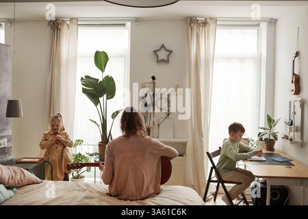 Rückansicht Porträt einer alleinerziehenden Mutter, die mit zwei Kindern auf dem Bett sitzt, in einem einfachen Wohnraum, Kopierraum Stockfoto