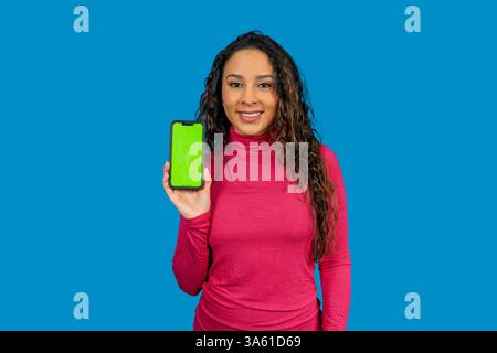 Lächelnde Frau zeigt ein Smartphone mit grünem Bildschirm, perfekt für die Präsentation von Apps oder Websites Stockfoto