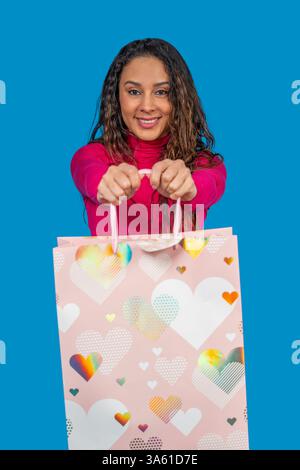 Lächelnde Frau zeigt eine rosa Einkaufstasche mit Herzen, bereit für den valentinstag oder einen besonderen Anlass Stockfoto