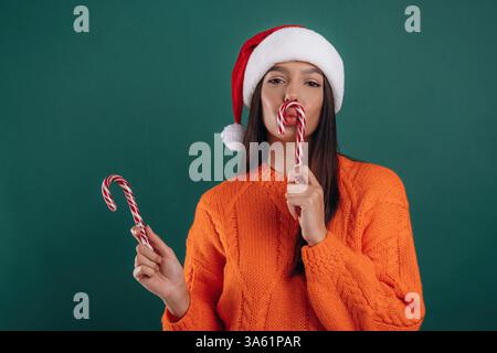 Süße Weihnachtsbonbons, mit Weihnachtsmütze. Die junge schöne Frau steht vor dem Hintergrund. Stockfoto