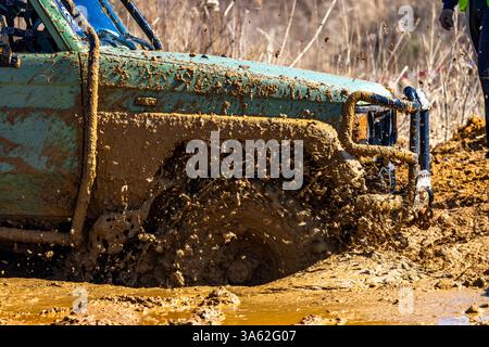 Ein grünes Geländefahrzeug steckt in einem riesigen Loch mit Schlamm und Wasser, überquert schwieriges Gelände mit dem Auto und tritt auf der Off-Road-Rennstrecke an Stockfoto