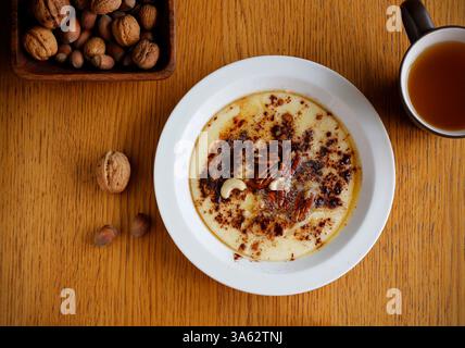 Gesunder glutenfreier Brei aus Buchweizen und Maisgrieß gekocht und auf weißem Teller mit Zimt, Ahornsirup, Butter und Nüssen serviert. Stockfoto