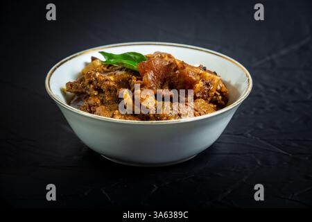 Rindfleisch Masala oder Braten, hausgemachtes Rezept nach Kerala-Art, garniert mit Curryblättern und in einer weißen Schüssel auf schwarzem Hintergrund serviert. Stockfoto