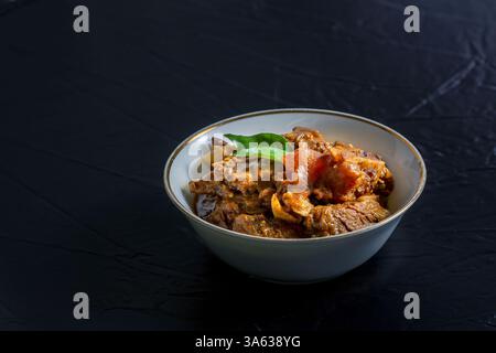 Rindfleisch Masala oder Braten, hausgemachtes Rezept nach Kerala-Art, garniert mit Curryblättern und in einer weißen Schüssel auf schwarzem Hintergrund serviert. Stockfoto