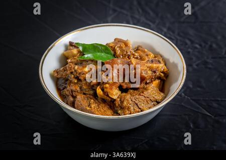 Rindfleisch Masala oder Braten, hausgemachtes Rezept nach Kerala-Art, garniert mit Curryblättern und in einer weißen Schüssel auf schwarzem Hintergrund serviert. Stockfoto