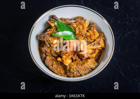 Rindfleisch Masala oder Braten, hausgemachtes Rezept nach Kerala-Art, garniert mit Curryblättern und in einer weißen Schüssel auf schwarzem Hintergrund serviert. Stockfoto