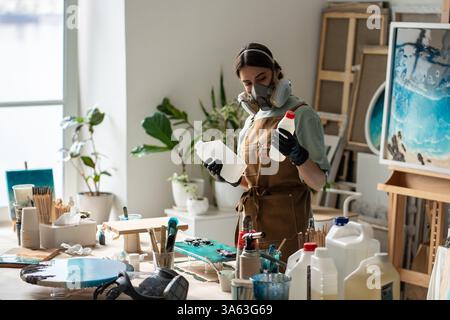 Die fokussierte Handwerkerin in Atemschutzgeräten verarbeitet Reagenzien, die Epoxidlösung für Kunstwerke im Studio vorbereiten Stockfoto