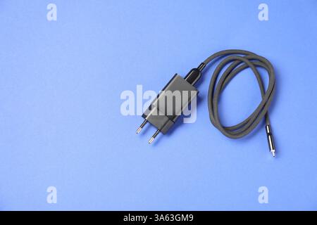 USB-Netzteil mit Ladekabel auf blauem Hintergrund, Draufsicht. Leerzeichen für Text Stockfoto