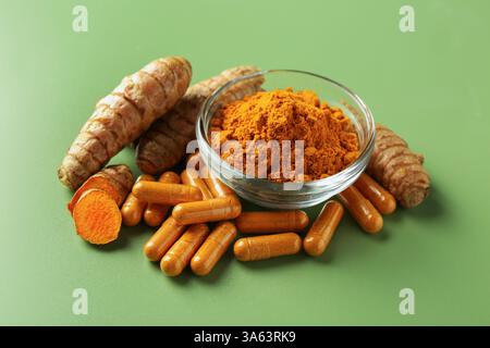 Kurkumapulver in Schüssel, Wurzeln und Kapseln auf grünem Hintergrund Stockfoto