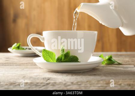 Frisch gebrühten Tee aus der Teekanne in eine Tasse am Holztisch gießen, Nahaufnahme Stockfoto