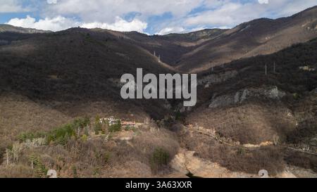 Aus der Vogelperspektive auf trockenes Flussbett und Stromleitungen durch ein Tal mit einem kleinen Dorf im Vordergrund Stockfoto