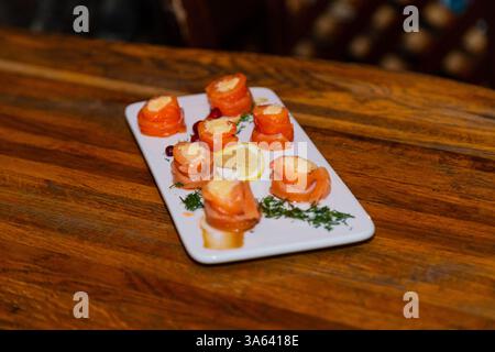 Appetitliche Fischbrötchen aus rotem Fisch mit Füllung im Inneren auf einem weißen Teller und einem Holztisch in einem Restaurant Stockfoto